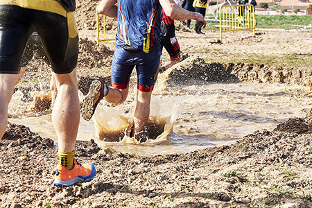 Obstacle Course Participants Running Through Mud